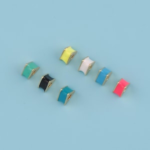 Puede incluir: Una colección de cuentas de esmalte coloridas con bordes dorados. Las cuentas son de varios colores, incluyendo turquesa, negro, amarillo, blanco, azul y rosa. Las cuentas están dispuestas sobre un fondo azul claro.