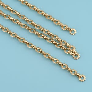 May include: Four gold-colored chains with a repeating floral-like pattern. Each chain has a small circular loop at the end. The chains are arranged diagonally against a light blue background.