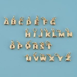 May include: Gold-colored alphabet charms, each with a small loop for attaching to a necklace or bracelet. The letters A through Z are displayed against a light blue background. These charms are ideal for personalized jewelry.