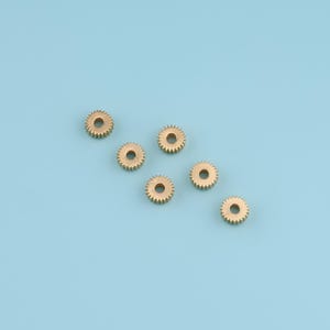 May include: Seven small, gold-colored gears with a central hole and toothed edges are arranged on a light blue background. The gears are evenly spaced, suggesting a mechanical or engineering theme.