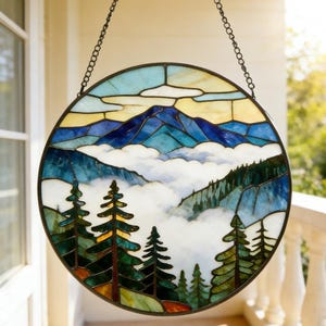 May include: Round stained glass panel depicting a mountain landscape with blue, green, and white hues. The design features a mountain range, clouds, and evergreen trees. The panel is suspended by a chain.