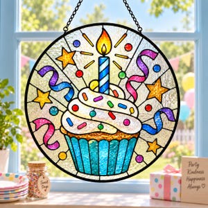 Puede incluir: Un atrapasoles circular de vidriera que muestra un cupcake con glaseado blanco, chispas de colores y una vela azul encendida. El diseño incluye estrellas amarillas, cintas rosas y azules, y pequeños círculos, dentro de un marco de metal negro.