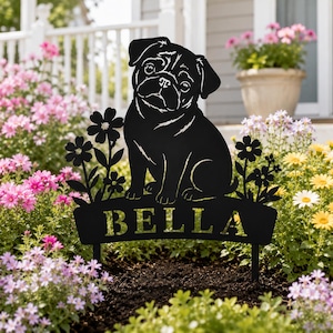 Könnte beinhalten: Ein schwarzer Gartenstecker aus Metall mit der Silhouette eines sitzenden Mopses inmitten stilisierter Blumen. Unter dem Hund befindet sich ein horizontales Banner, in das der Name BELLA in Großbuchstaben eingestanzt ist.