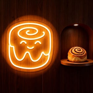 May include: A neon sign in the shape of a smiling cinnamon roll, glowing with a warm orange light, is mounted on a wooden wall. To the right, a fresh cinnamon roll sits on a wooden shelf, illuminated by a small spotlight.