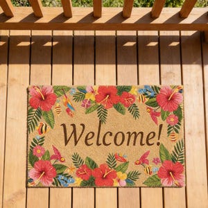 May include: A rectangular doormat with a tan background and the word "Welcome!" in brown script. The mat is decorated with red hibiscus flowers, green leaves, and colorful birds.