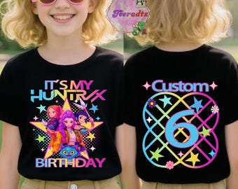 May include: Black t-shirt with a colorful graphic design. The front features the text "IT'S MY HUNTRIX BIRTHDAY" with cartoon characters. The back has "Custom" and the number "6" in a star and flower design.
