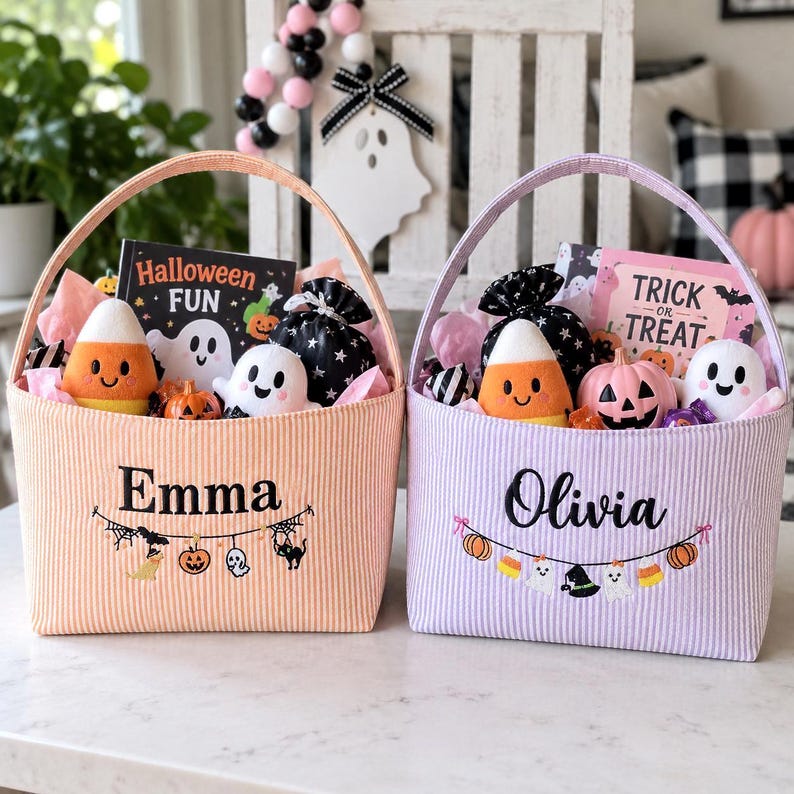 Puede incluir: Dos cestas de tela con asas, una naranja y otra lavanda, con los nombres bordados Emma y Olivia. Cada cesta contiene peluches que incluyen un fantasma y un caramelo de ma&iacute;z, una peque&ntilde;a calabaza y un libro titulado Halloween Fun o Trick or Treat.