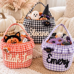 Puede incluir: Tres cestas de Halloween de tela con bordes con volantes y patrones de cuadros vichy en negro, naranja y morado. Cada cesta presenta un nombre personalizado en letras en relieve: Sloane, Lilah Love y Emery, decoradas con peluches de fantasmas, murciélagos y calabazas.