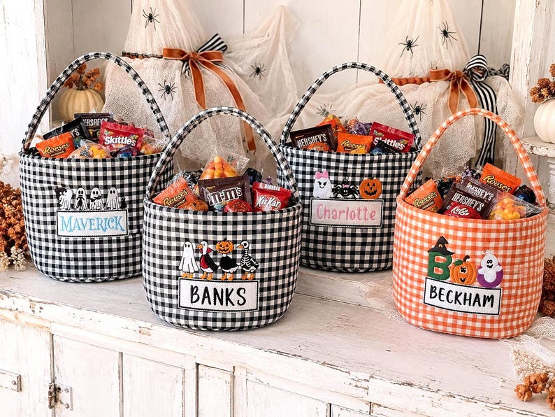 Puede incluir: Cuatro cestas de tela con asas, tres de cuadros vichy en blanco y negro y una en blanco y naranja. Cada cesta presenta motivos bordados de Halloween y una etiqueta rectangular con los nombres Maverick, Banks, Charlotte y Beckham.