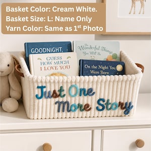May include: A cream white rectangular storage basket with brown leather-like handles. The front features the embroidered text "Just One More Story" in blue and brown yarn. Inside the basket are four children's books titled Goodnight, Guess How Much I Love You, The Wonderful Things You Will Be, and On the Night You Were Born.