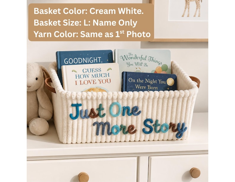 May include: A cream white rectangular storage basket with brown leather-like handles. The front features the embroidered text "Just One More Story" in blue and brown yarn. Inside the basket are four children's books titled Goodnight, Guess How Much I Love You, The Wonderful Things You Will Be, and On the Night You Were Born.