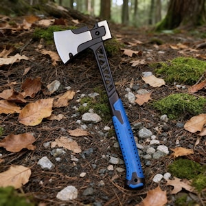 May include: A black and silver hatchet with a blue handle lies on a forest floor. The hatchet has a silver blade, a black head, and a blue, textured handle. The background shows a forest floor with leaves and moss.