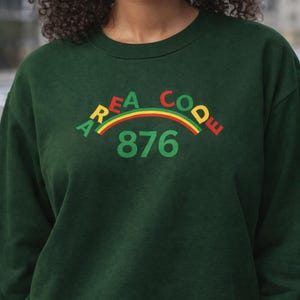 May include: Dark green sweatshirt with the text "AREA CODE 876" in a rainbow arc design. The sweatshirt is a solid color and has a crew neck.