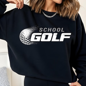 Puede incluir: Sudadera negra con las palabras "SCHOOL GOLF" en letras blancas y un gráfico de pelota de golf blanca. El gráfico de la pelota de golf está parcialmente fragmentado, creando un efecto visual dinámico. La sudadera es de color negro sólido.