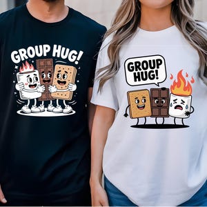 Puede incluir: Camisetas negras y blancas con un dibujo animado de una nube de azúcar, una tableta de chocolate y una galleta abrazándose. El texto "GROUP HUG!" está encima del dibujo en la camiseta negra y en un bocadillo en la camiseta blanca. La nube de azúcar tiene llamas.