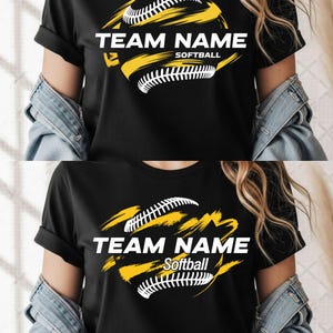 May include: Black t-shirt featuring a softball design with the words "TEAM NAME" and "Softball" in white. The design includes a yellow and white softball graphic. The shirt has short sleeves.