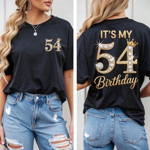 May include: Black t-shirt with the number "54" and a crown design. The front of the shirt has a small "54" with a crown. The back of the shirt says "IT'S MY 54 Birthday" in gold lettering.