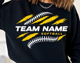 May include: Black sweatshirt with a softball design. The design features a white softball with yellow slashes and the words "TEAM NAME SOFTBALL" in white block letters.