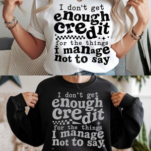 Könnte beinhalten: Zwei T-Shirts, eines weiß und eines schwarz, mit dem Text "I don't get enough credit for the things I manage not to say". Der Text ist in einer fetten, stilisierten Schriftart.