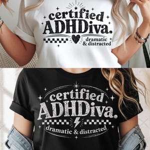Puede incluir: Dos camisetas, una blanca y otra negra, muestran el texto "certified ADHDiva. dramatic & distracted" en colores contrastantes. El diseño incluye un corazón, estrellas y un patrón de tablero de ajedrez.