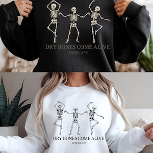 Peut inclure: Sweat-shirts noirs et blancs avec un motif de trois squelettes dansants. Le texte "DRY BONES COME ALIVE" et "EZEKIEL 37:5" sont imprimés en dessous. Un sweat-shirt est noir, l'autre est blanc.