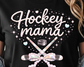 Puede incluir: Camiseta negra con la frase "Hockey Mama" en cursiva. El diseño incluye palos de hockey cruzados, un disco y un lazo. El diseño está acentuado con estrellas y corazones.