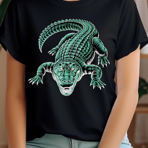 Puede incluir: Camiseta negra con una ilustración detallada de un caimán verde. El caimán se representa con dientes y garras afiladas, y su cuerpo está cubierto de escamas texturizadas. El diseño está centrado en la camiseta, creando un gráfico audaz.