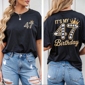 May include: Black t-shirt with the number "47" and a crown design. The front of the shirt has the number "47" with a crown. The back of the shirt says "IT'S MY 47 BIRTHDAY" in gold lettering.