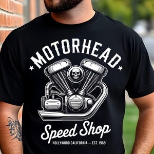 Peut inclure: T-shirt noir avec un motif de moteur de moto détaillé, orné d'un crâne. Le texte "MOTORHEAD" surplombe le moteur, avec "Speed Shop" et "HOLLYWOOD CALIFORNIA - EST. 1969" en dessous. Un design classique.