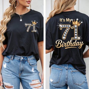 Puede incluir: Camiseta negra con un diseño dorado y pedrería "71" y una corona. La parte delantera de la camiseta presenta el número "71" con una corona. La parte trasera de la camiseta dice "It's My 71st Birthday" en letras doradas.