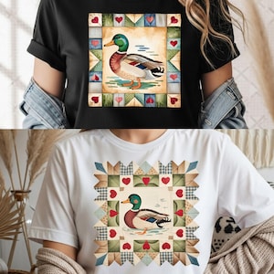 Peut inclure: T-shirt noir avec une illustration à l'aquarelle d'un canard colvert dans un motif de patchwork. Le canard a des plumes vertes, marron et blanches, avec un bec jaune. La bordure du patchwork comprend des cœurs et des motifs géométriques.