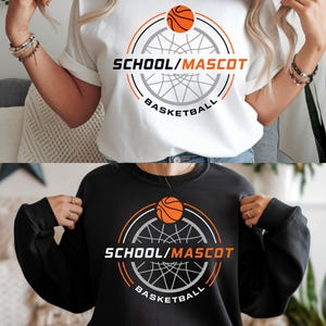 Peut inclure: T-shirt blanc et sweat-shirt noir avec un motif de basket-ball. Le motif comprend un ballon de basket au-dessus du texte "SCHOOL/MASCOT BASKETBALL" en noir et orange. Les deux articles sont à manches courtes.