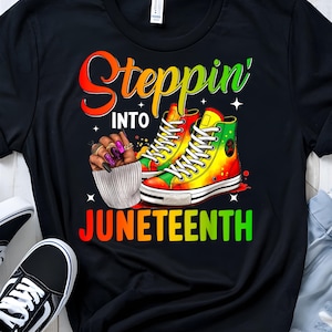 Peut inclure: T-shirt noir avec le texte "Steppin' into Juneteenth" en couleurs arc-en-ciel. Le design présente une paire de baskets colorées et une main avec des ongles peints.