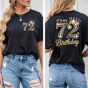 Puede incluir: Camiseta negra con diseño dorado y pedrería. El frente presenta el número 72 con una corona, y la parte trasera dice "IT'S MY 72 BIRTHDAY" en letras doradas. La camiseta se combina con vaqueros azules.