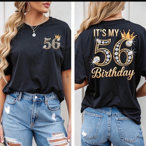 May include: Black t-shirt with a gold and rhinestone "56" design and a small crown. The back of the shirt features the text "IT'S MY 56 BIRTHDAY" in gold script with a crown.