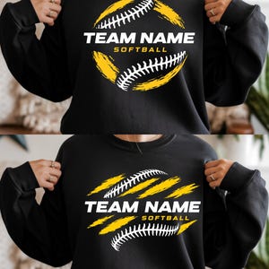 May include: Black sweatshirt featuring a softball design. The design includes a yellow and white softball graphic with the text "TEAM NAME SOFTBALL" in white. The sweatshirt is a crew neck style.
