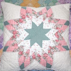 May include: Square white quilted pillow with a large star design. The star features a central teal section with a white polka dot pattern, surrounded by pink floral and gingham patterned sections.