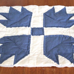 May include: A handmade quilt block featuring a central square and four stylized bear paw designs in navy blue. The bear paw shapes are set against a white background, with a teal border. The quilt block is likely part of a larger quilt.