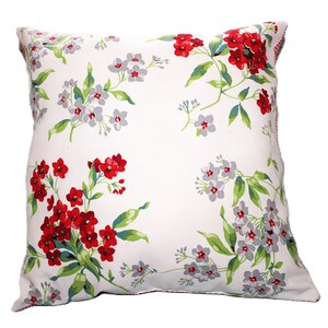 May include: Square white pillow with a floral pattern. The design features clusters of red and gray flowers with green leaves, set against a white background. The pillow's edges have a red and white checkered trim.