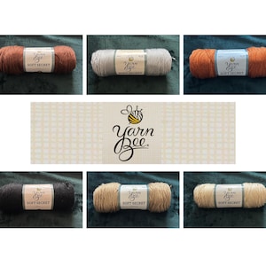 May include: A collection of Yarn Bee Soft Secret yarn skeins in various colors, including brown, gray, and orange. Each skein has a label with the brand name and product details. The image also features a Yarn Bee logo.