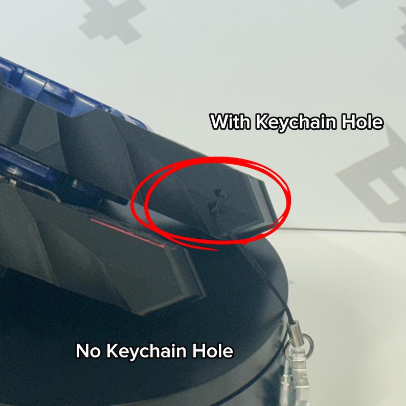 Pu&ograve; includere: Primo piano di un oggetto nero e blu con il testo "With Keychain Hole" e "No Keychain Hole". L'immagine evidenzia un piccolo foro per un portachiavi.