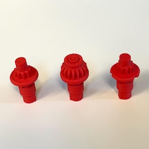 May include: Three red plastic gears with a detailed design. The gears are different sizes and are arranged in a row on a white surface.