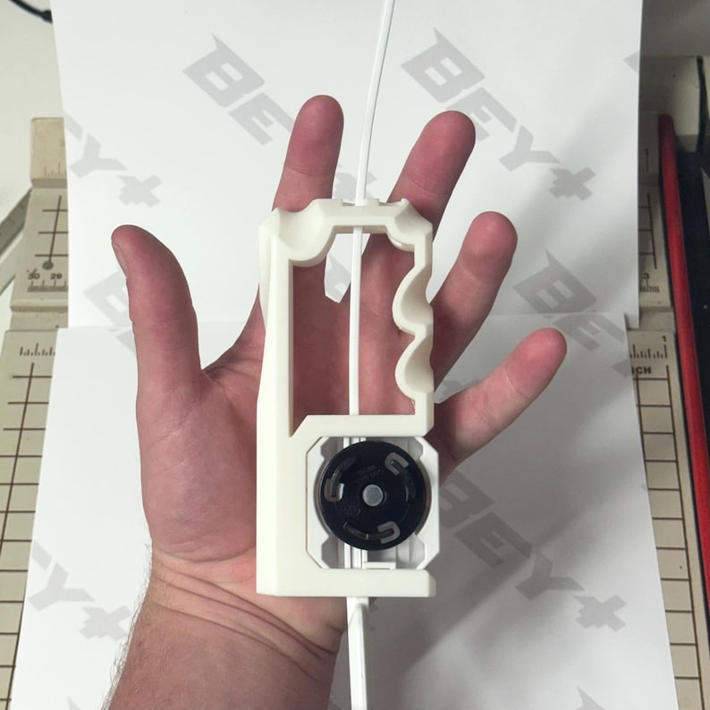May include: A white 3D-printed plastic launcher tool featuring a vertical handle with ergonomic finger grooves and a circular black gear mechanism at the base. A thin white plastic strip is inserted through the center of the device.