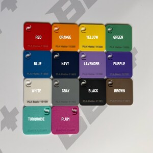 May include: A collection of fourteen square plastic filament swatches arranged in a grid. Each swatch features a color name, such as red, orange, yellow, green, blue, navy, lavender, purple, white, gray, black, brown, turquoise, and plum.