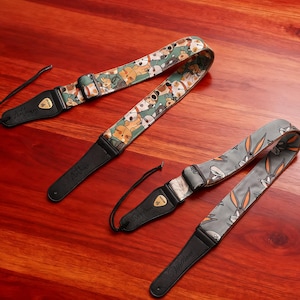 Peut inclure: Trois sangles de guitare avec des extrémités en cuir noir et des motifs en tissu coloré. L'une présente un motif de chiens de dessin animé sur fond vert. Une autre a un motif Bugs Bunny sur fond gris. La troisième a un motif de chien de dessin animé.