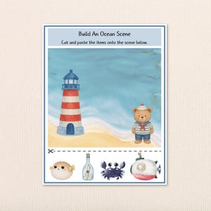 May include: A children's activity sheet titled "Build An Ocean Scene." It features a lighthouse, a teddy bear in a sailor outfit, and cut-out images of sea creatures. The background shows a beach and ocean.