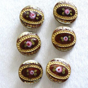 May include: Six antique buttons with a floral design. Each button features a central oval with a pink rose and green leaves, surrounded by a gold border and a dark brown background. The buttons are set against a white background.
