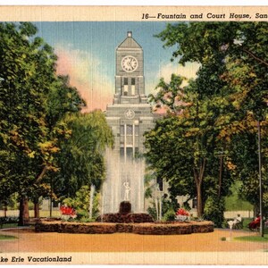 May include: A vintage postcard featuring a colorized illustration of the Fountain and Court House in Sandusky, Ohio. The scene depicts a central stone fountain spraying water in front of a tall clock tower building, surrounded by lush green trees.