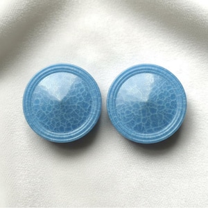 May include: Two round, light blue decorative objects with a textured, cracked pattern on the surface. Each object has a raised, circular border. The objects are displayed on a white background.