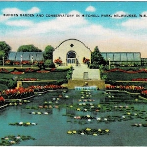 May include: Vintage postcard featuring the Sunken Garden and Conservatory in Mitchell Park, Milwaukee, Wisconsin. The image shows a pond with lily pads, flower beds, and a building with a glass greenhouse. The sky is blue with white clouds.
